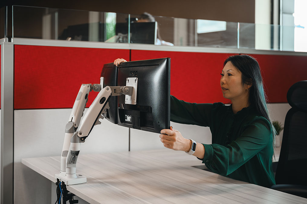 office worker adjusting monitor arms for ergonomic desk